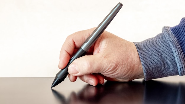 A man holds a pen a stylus and draws with a graphics tablet