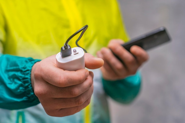 Man holds a power bank in his hands and charges a smartphone against a concrete wall