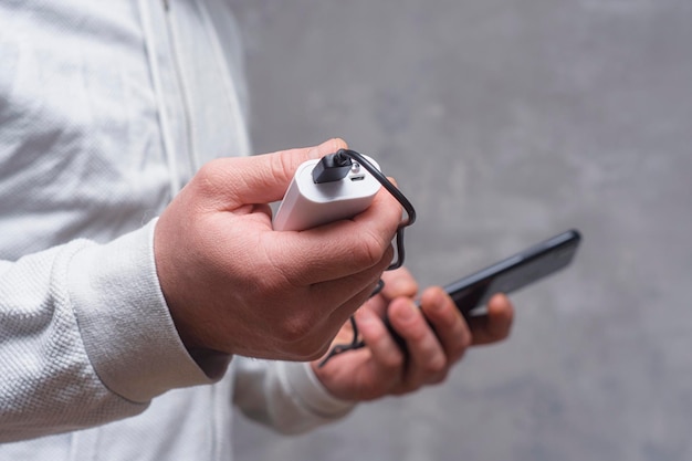 Man holds a power bank in his hands and charges a smartphone against a concrete wall