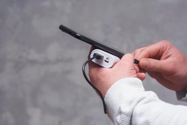 Man holds a power bank in his hands and charges a smartphone against a concrete wall