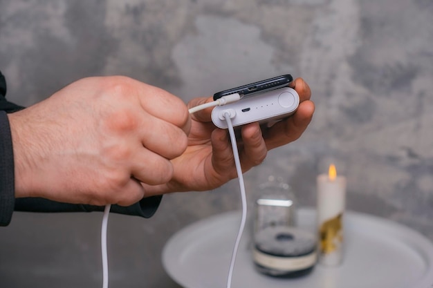 Man holds a power bank in his hands and charges a smartphone against a concrete wall