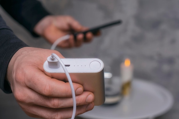 Man holds a power bank in his hands and charges a smartphone against a concrete wall