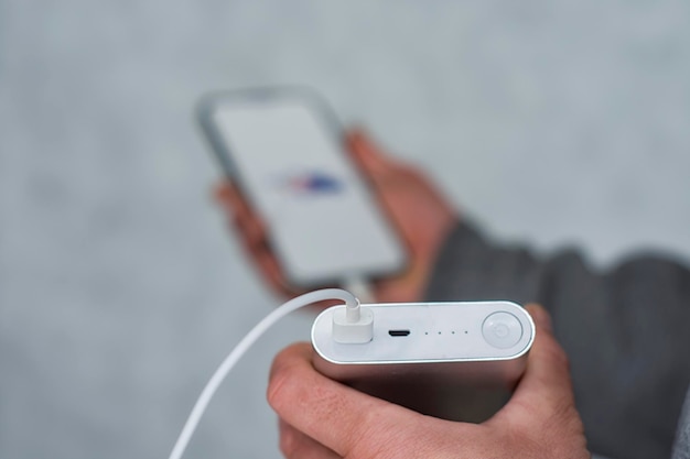 A man holds a power bank in his hands and charges smartphone on a gray background.