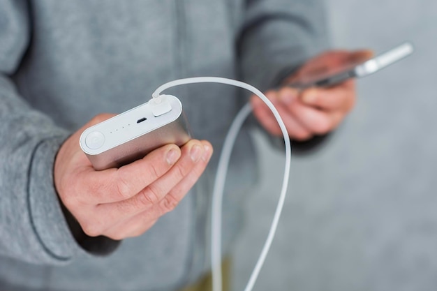 A man holds a power bank in his hands and charges smartphone on a gray background.