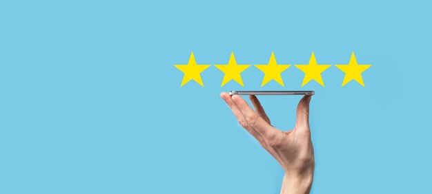 Man holds smart phone in hands and gives positive rating, icon five star symbol to increase rating of company concept on blue background.Customer service experience and business satisfaction survey.