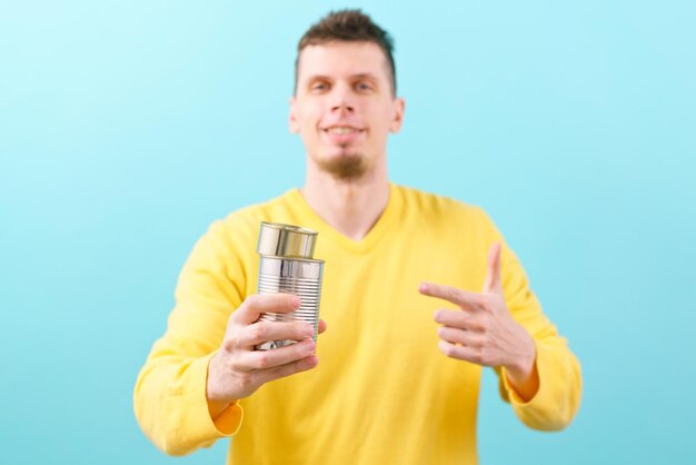 A man holds two steel cans and points his finger at them on a blue. Canned food Recycle