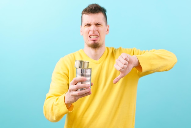 A man holds two steel cans and shows his thumb down on a blue. Tinned. Tincan