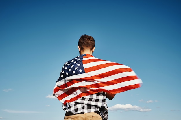 Man holds usa national flag against blue cloudy sky