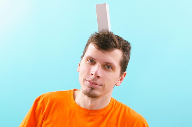 A man holds a white cardboard box template on his head and smiling on a blue. Promotion