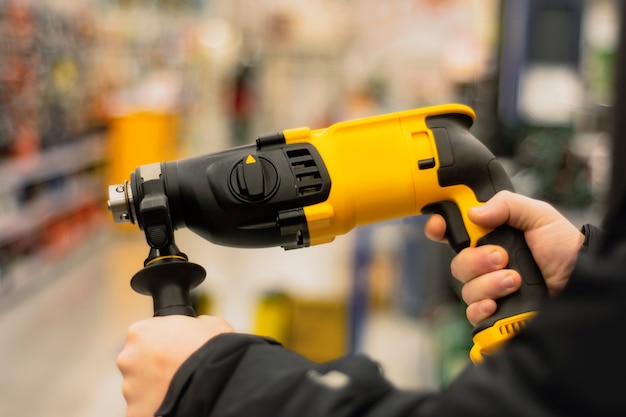 Man holds a yellow puncher for repair work in his hands against the backdrop of showcases in a hardware store.