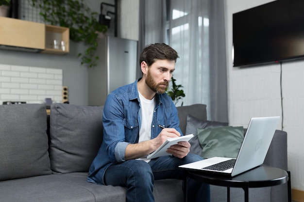 The man at home is studying remotely uses a laptop sitting at home on the couch recording a lecture