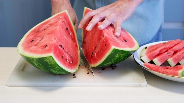 Man in home kitchen while cutting a ripe red watermelon in slices