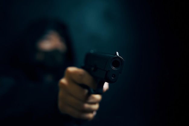 Man in hood threatens with firearm masked robber with gun weapon in persons hands murderer or armed ...