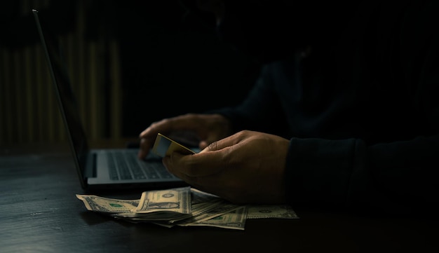 man in a hoodie using a laptop to hack credit card financial informatio