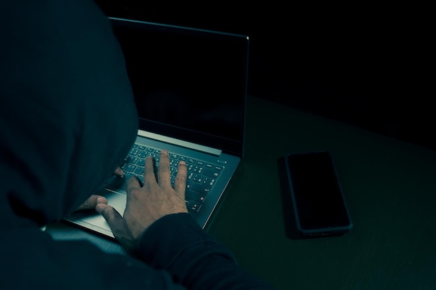 man in a hoodie using a laptop to hack credit card financial informatio