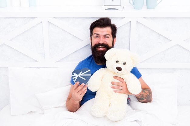 Man hug soft toy relaxing in bed. Make surprise concept. Gift for spouse. Cute and romantic gift. Bearded hipster prepare lovely gift. Valentines day gift. Spread love. Present for sweetheart.