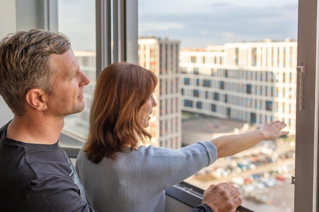 Man hugging his wife Young couple moving in new apartmen People looks out window at new houses Concept new homes new beginning