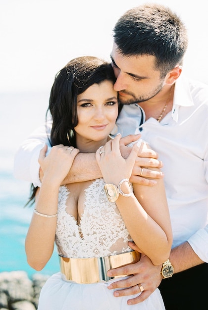 Man hugging a woman in a white dress by the shoulders from behind