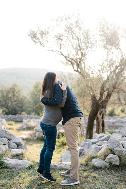 Man hugs pregnant woman standing on tiptoe in park