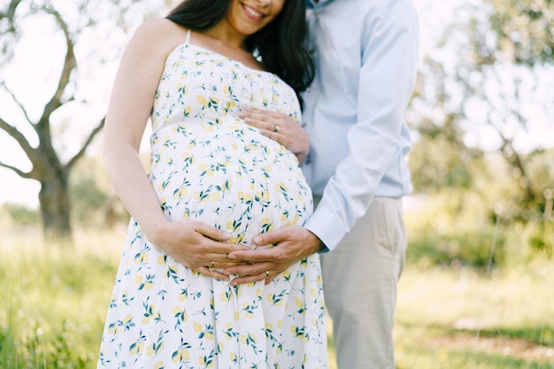 Man hugs a woman pregnant belly in the park closeup