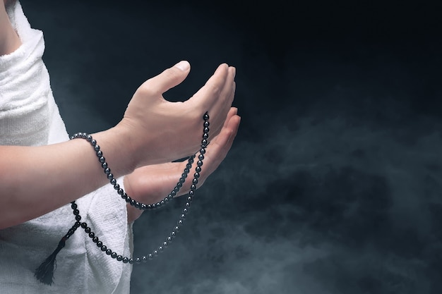 man in ihram clothes praying with prayer beads on his hands