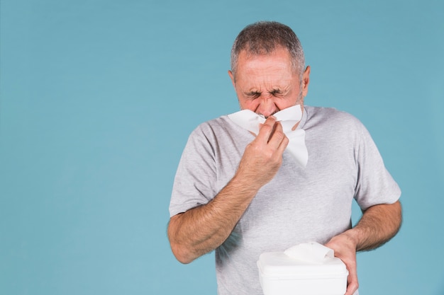 Man infected with cold and flu blowing his nose in tissue