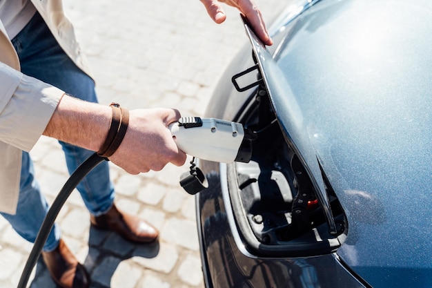 Man inserts plug of the charger into the socket of electric car