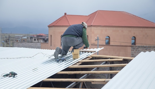 Man installing of sheets of metal tiles of roof