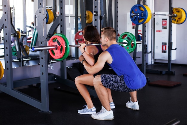 Man instructor securing woman with the barbell