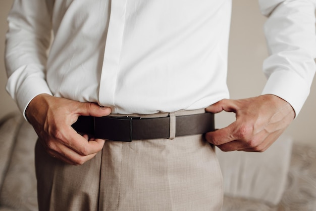 A man is adjusting his belt while wearing a white shirt