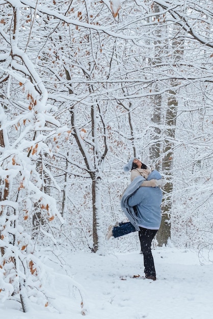 The man is circling the woman in his arms in a snowy forest