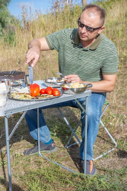 A man is cooking in a campfire in the grass.