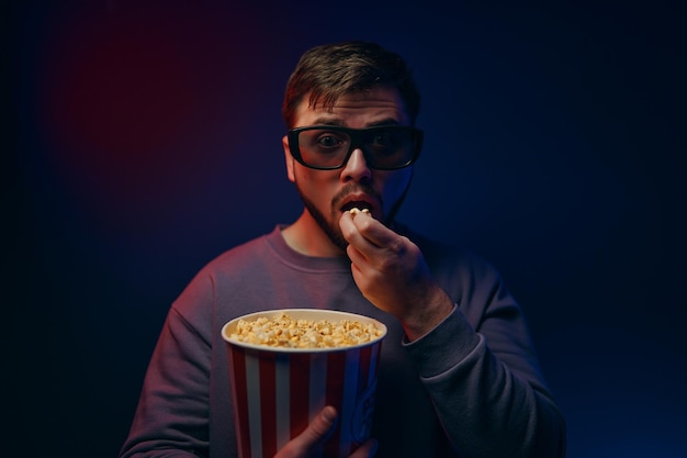 A man is in a dark room with neon lighting watching a movie with d glasses and popcorn high quality