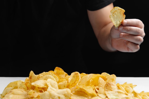 The man is eating junk food chips on a dark background harmful food fried food is bad for your healt