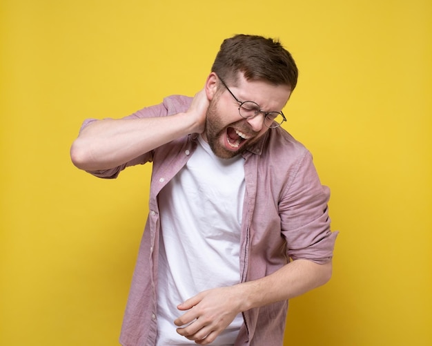 Man is experiencing severe pain in the neck area he holds hand to inflamed area and screams