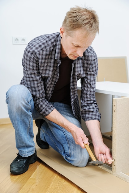 The man is hammering a wooden pin into a furniture board.