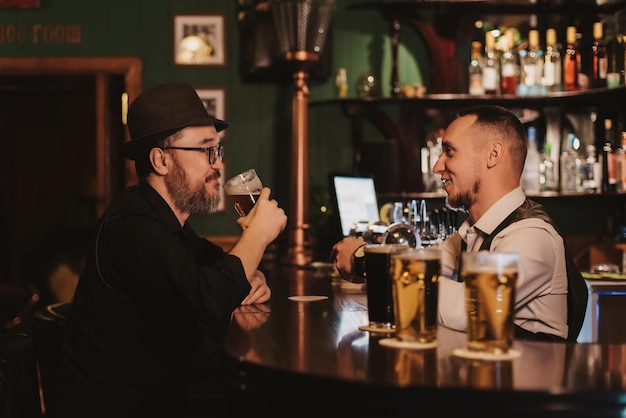 Man is having fun chatting with a bartender in bar counter while drinking beer from a glass