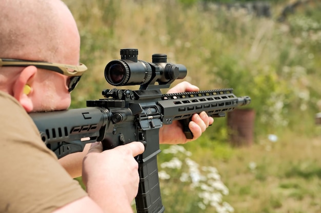 A man is holding an automatic weapon a man looks into the sight of a military weapon