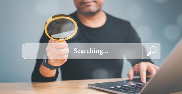 Photo a man is holding a magnifying glass over a laptop screen that says searching