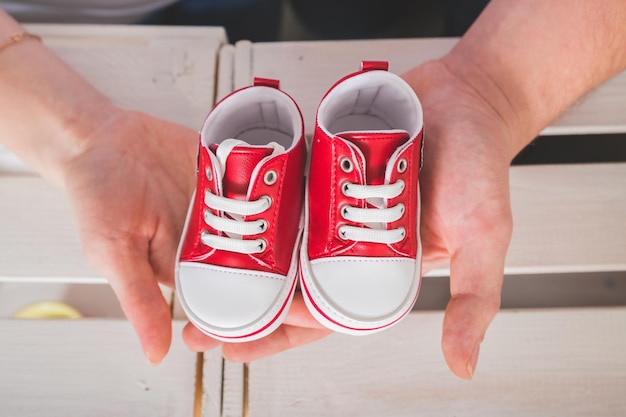 Man is holding small red leather shoes in hands Young white family waiting birth of their first baby dreaming about son or daughter Happy parents conceptsmall sneakers in palms