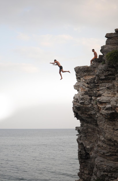 A man is jumping from a high cliff into the sea