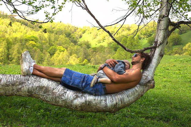 Photo a man is laying in a tree with a baby on his lap