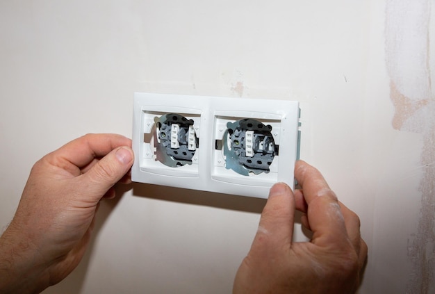 Man is making socket switches in wall Maintenance repair works in the flat Renovation indoors