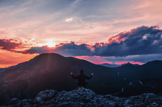 Man is meditating in the mountains at sunset.