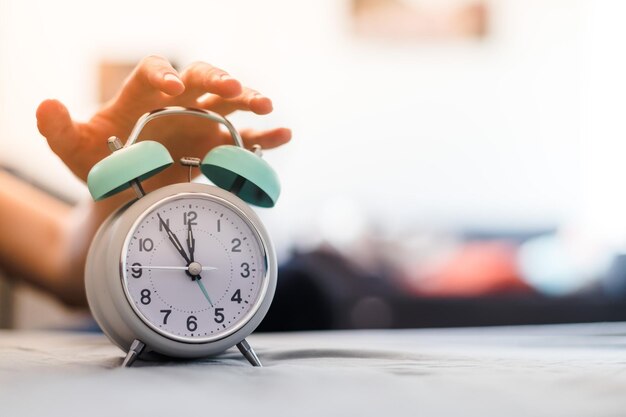 Man is pushing an alarm clock in the morning sunshine and blurry background