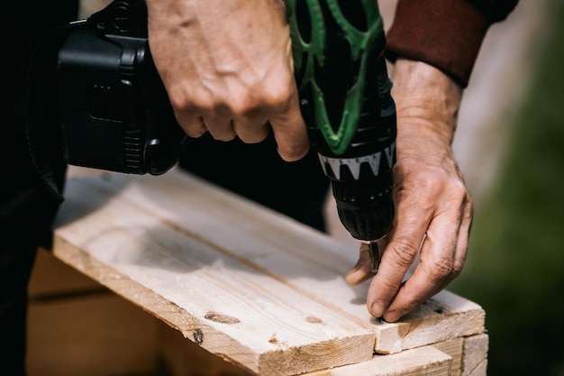 Man is screwing screw into wooden box with cordless screwdriver Product repair with professional tool electric screwdriver Close up