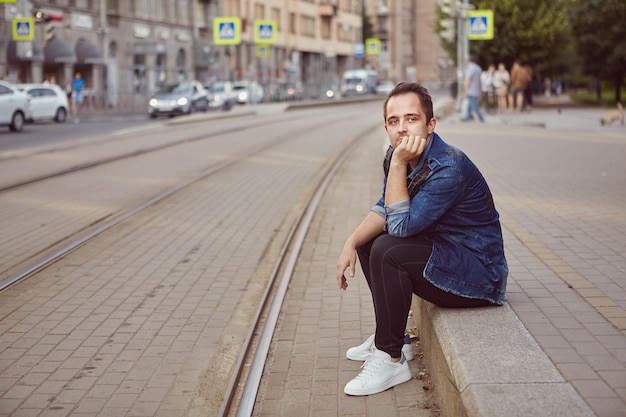 Man is sitting on sidewalk near  railroad.