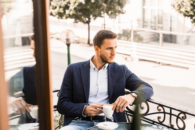 Man is sitting on the summer terrace in cafe drinking coffee and smiling Handsome man with coffee