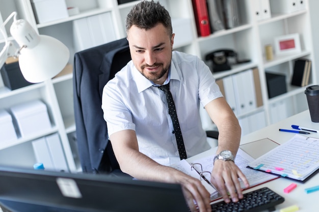 A man is sitting at a table in the office, working with documents and a computer.