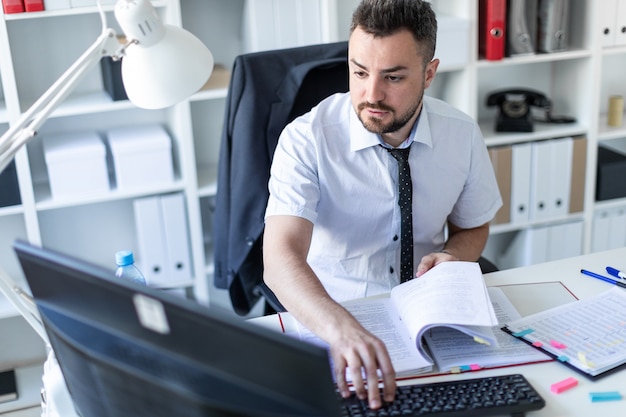 A man is sitting at a table in the office, working with documents and a computer.